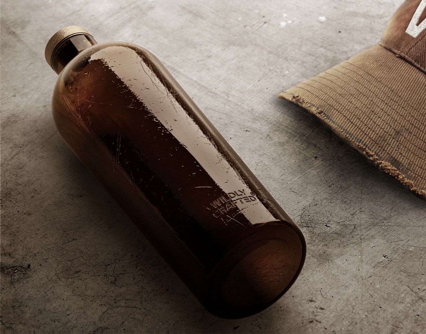 Estal Wildly Crafted Náladový obrázek: hnědá láhev kolekce Wildly Crafted leží na šedém betonovém pozadí, vedle ní hnědá čepice s kšiltem